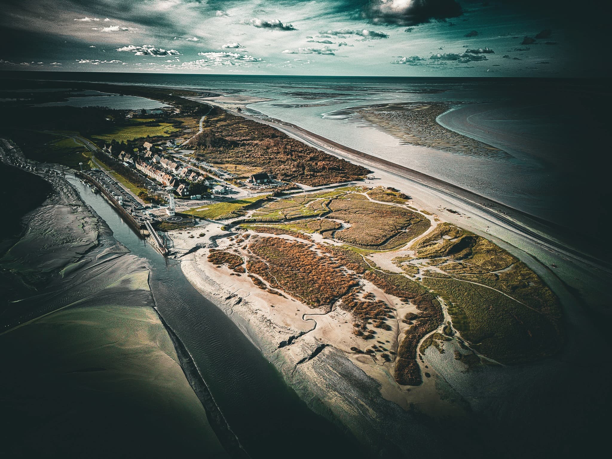 Phare blanc et vert du Hourdel à marée basse avec phoques visibles sur les bancs de sable au coucher du soleil